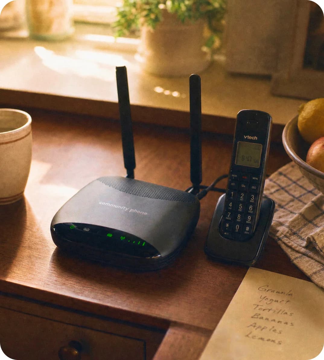 Community Phone Base and cordless handset on a kitchen table next to a handwritten grocery list