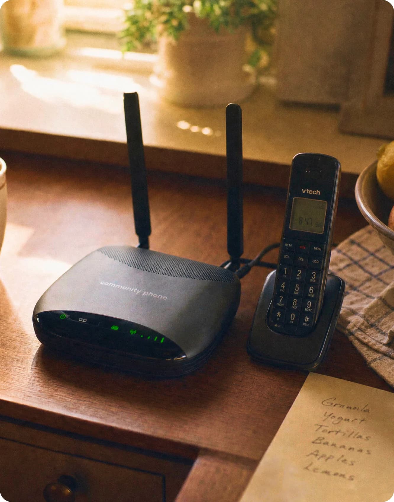 Community Phone Base and cordless handset on a kitchen table next to a handwritten grocery list