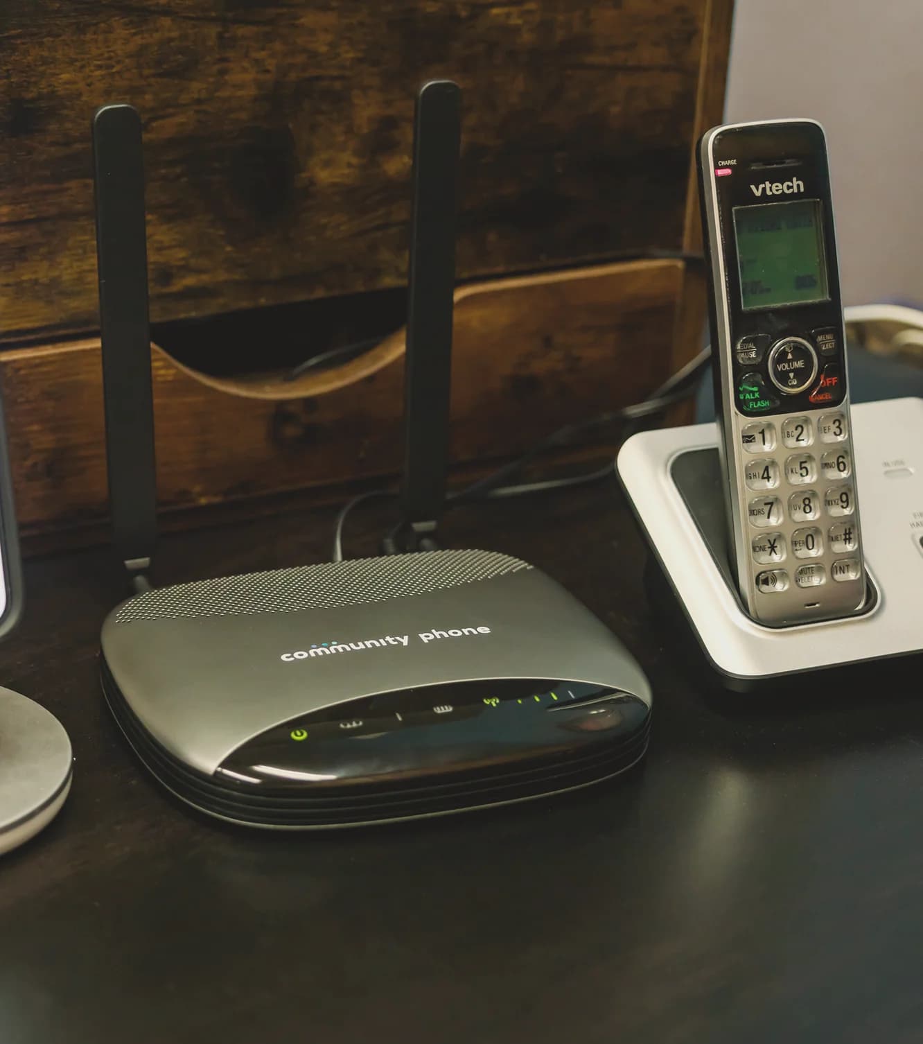 Community Phone Base between a phone showing the app and a cordless handset on a desk